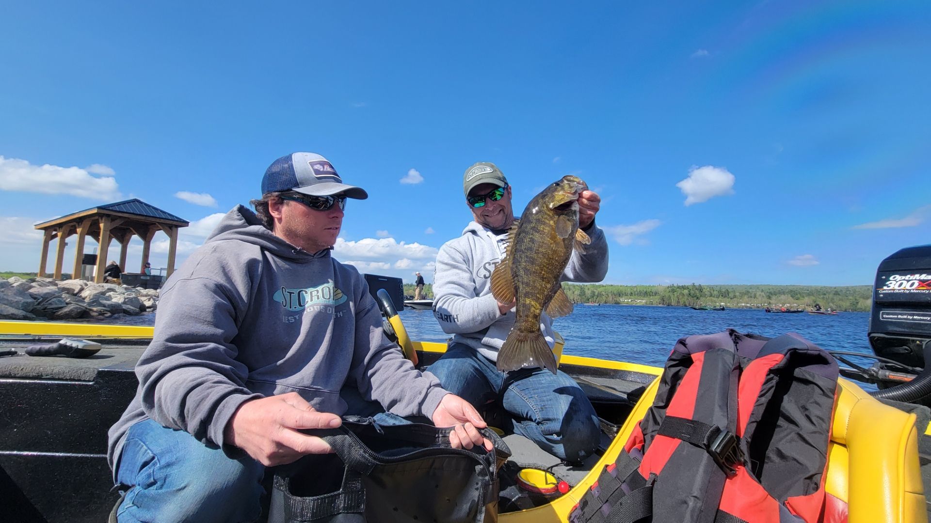 Two men on a boat, one holding a large fish. Sunny day on the water.