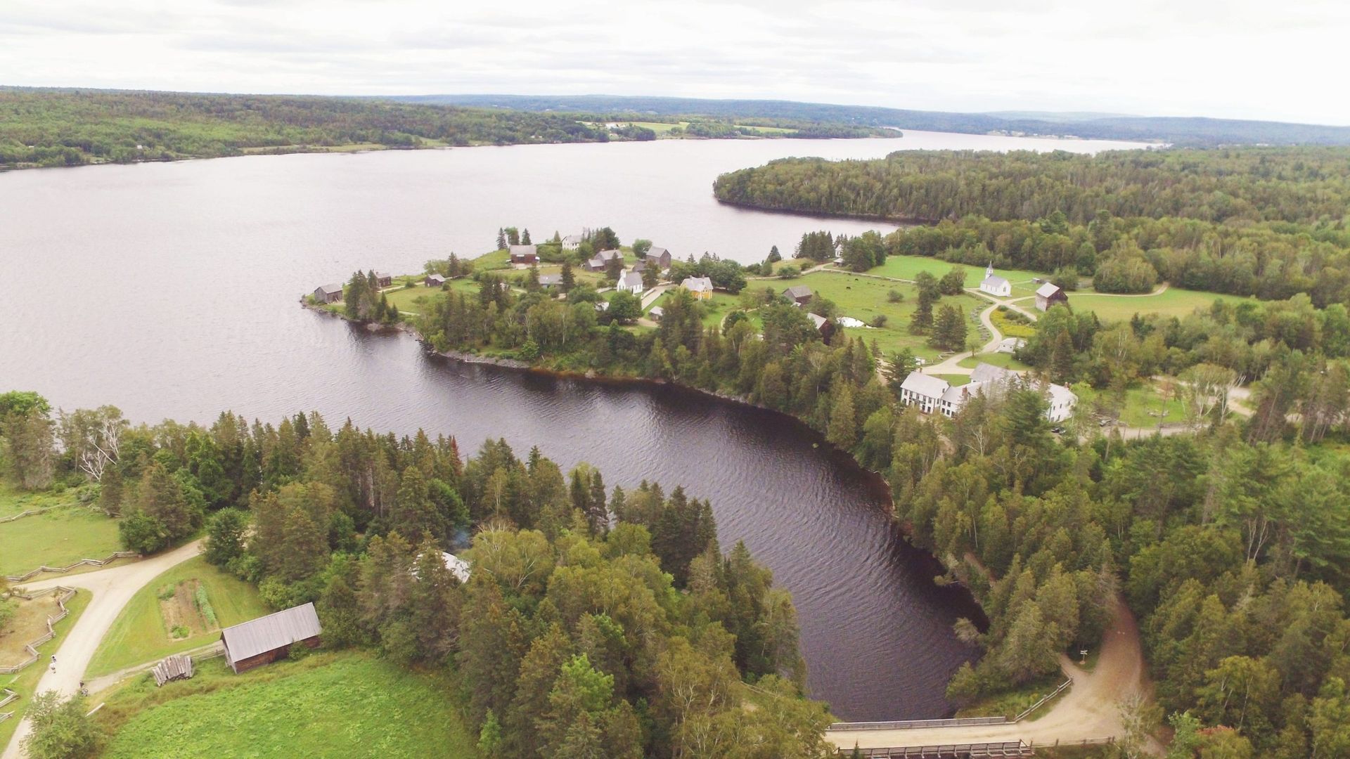 Aerial view of a lake surrounded by green trees and land, with small buildings visible on the shore.