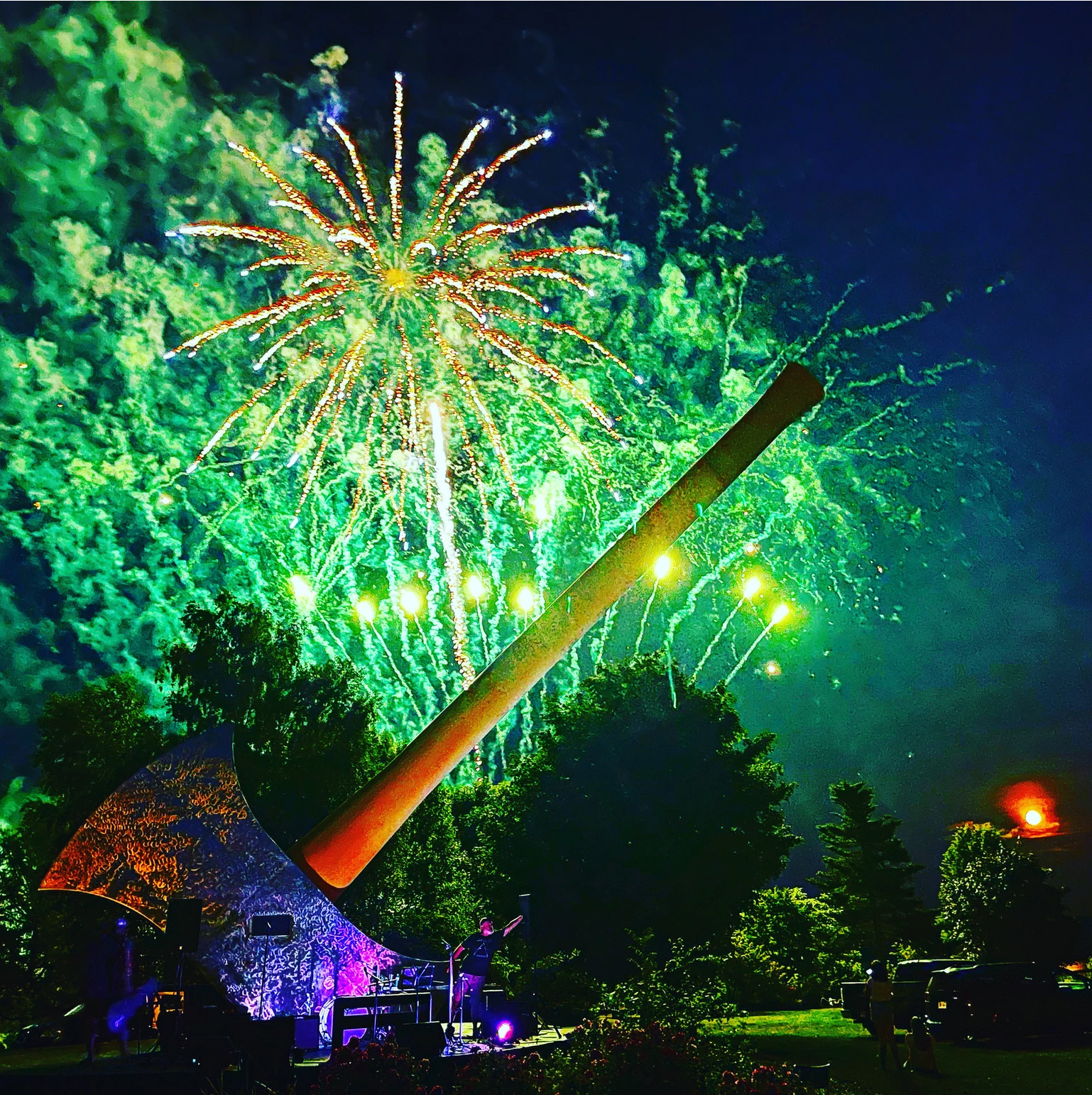 Fireworks over a large axe sculpture at night. Green and gold explosions over the illuminated axe.