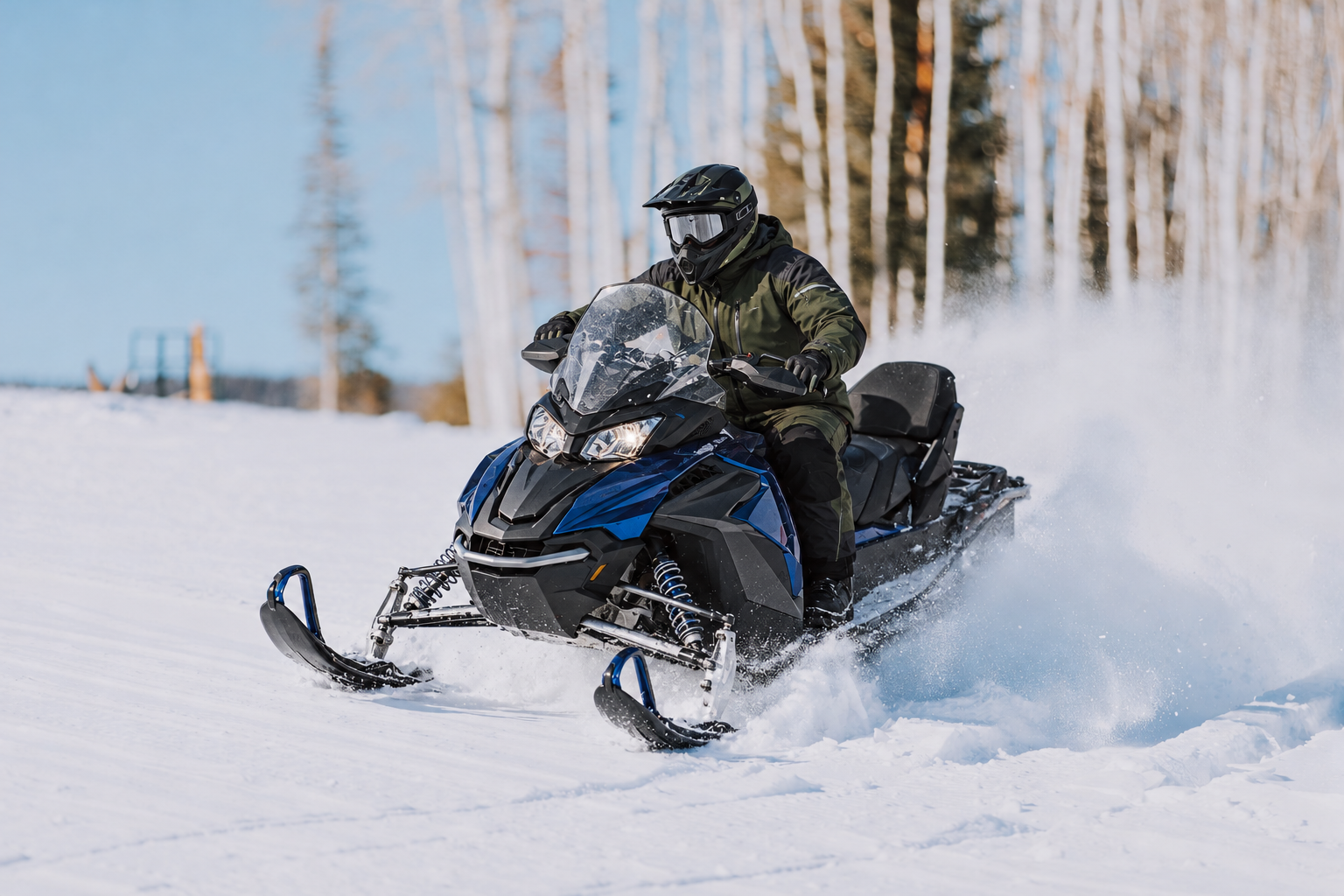 Snowmobiler in green winter gear riding a blue and black sled through fresh snow on a wooded trail.