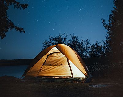 A group of people are standing around a campfire in front of a rv.