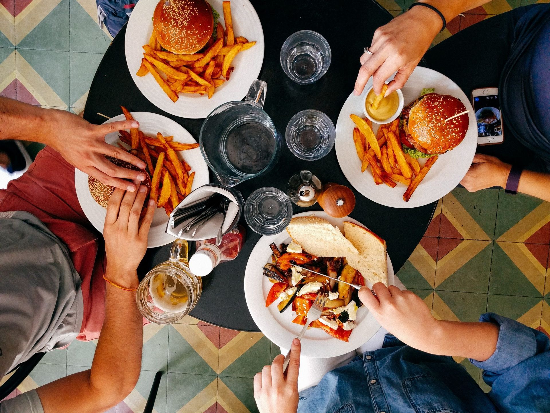 People sharing burgers and fries around a table with drinks, viewed from above.