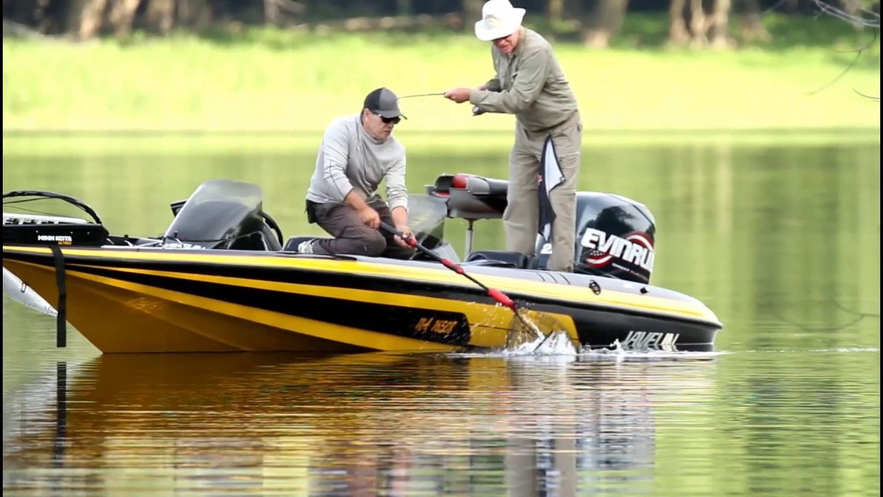 Two people fishing from a yellow boat on a lake. One kneels to net a fish.
