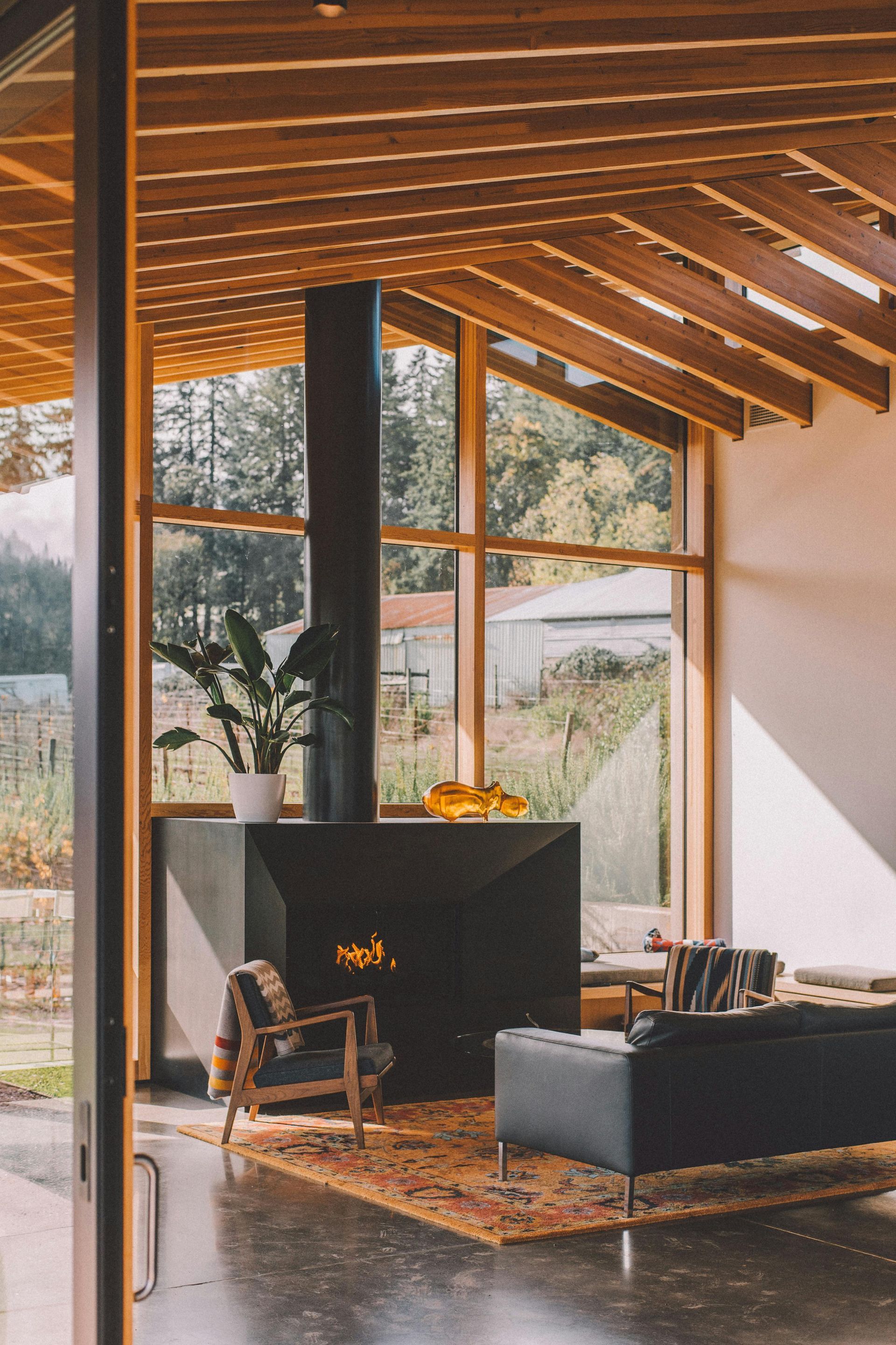 Modern living room with fireplace, wood ceiling, large windows, and outdoor view.