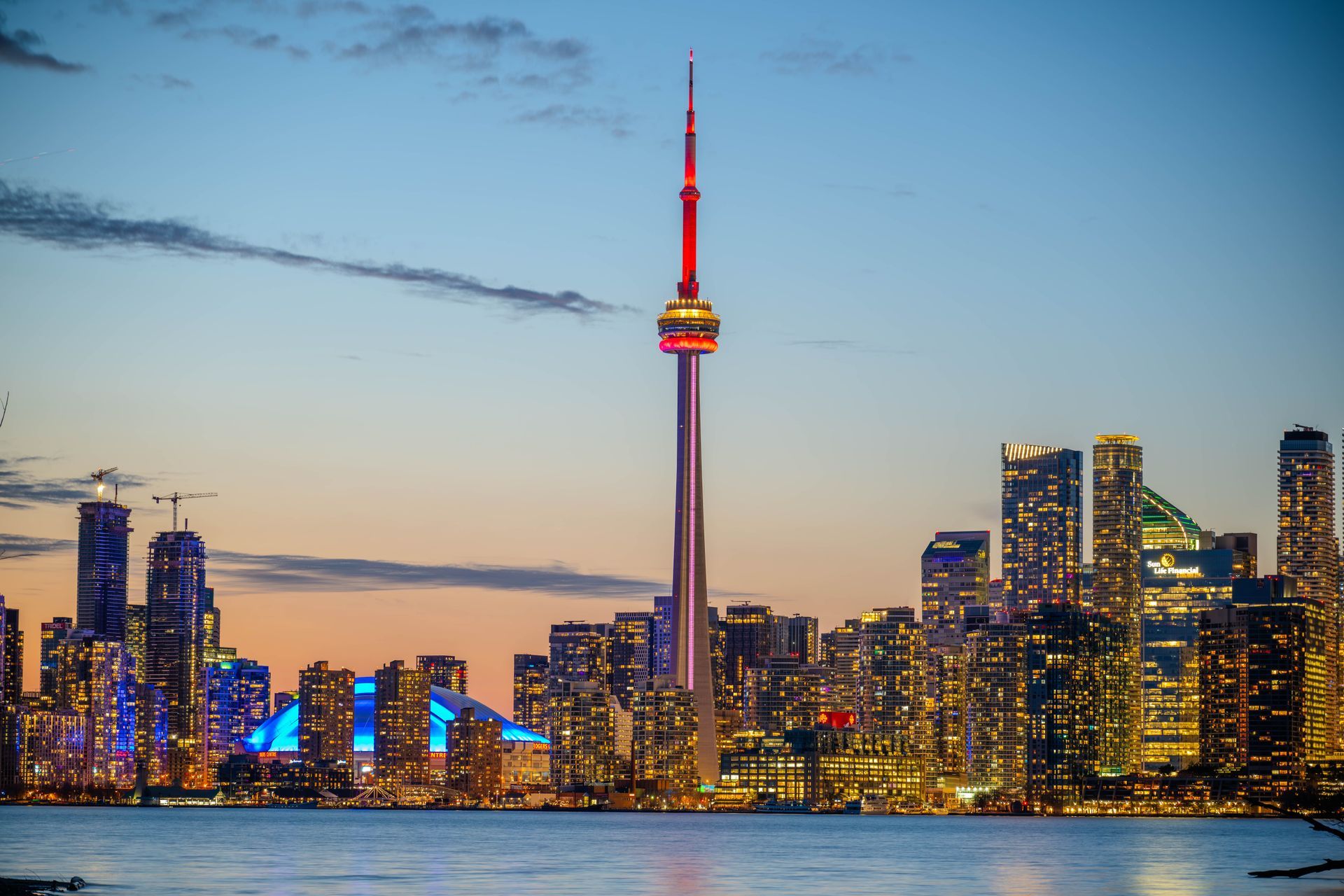 Toronto skyline at dusk with the CN Tower lit red above city lights and water