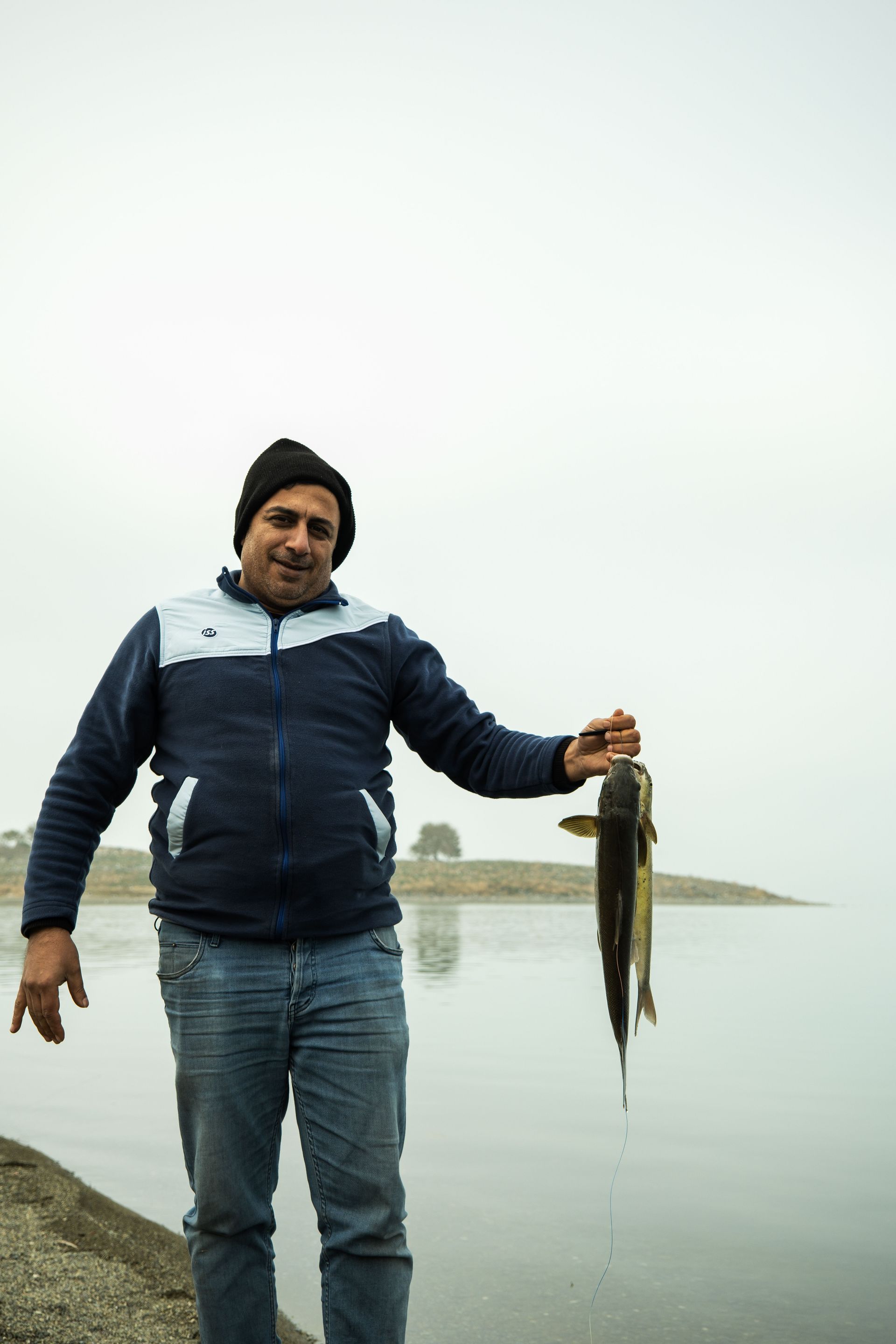 Man standing by the water holding a fish, with a small island in the background.