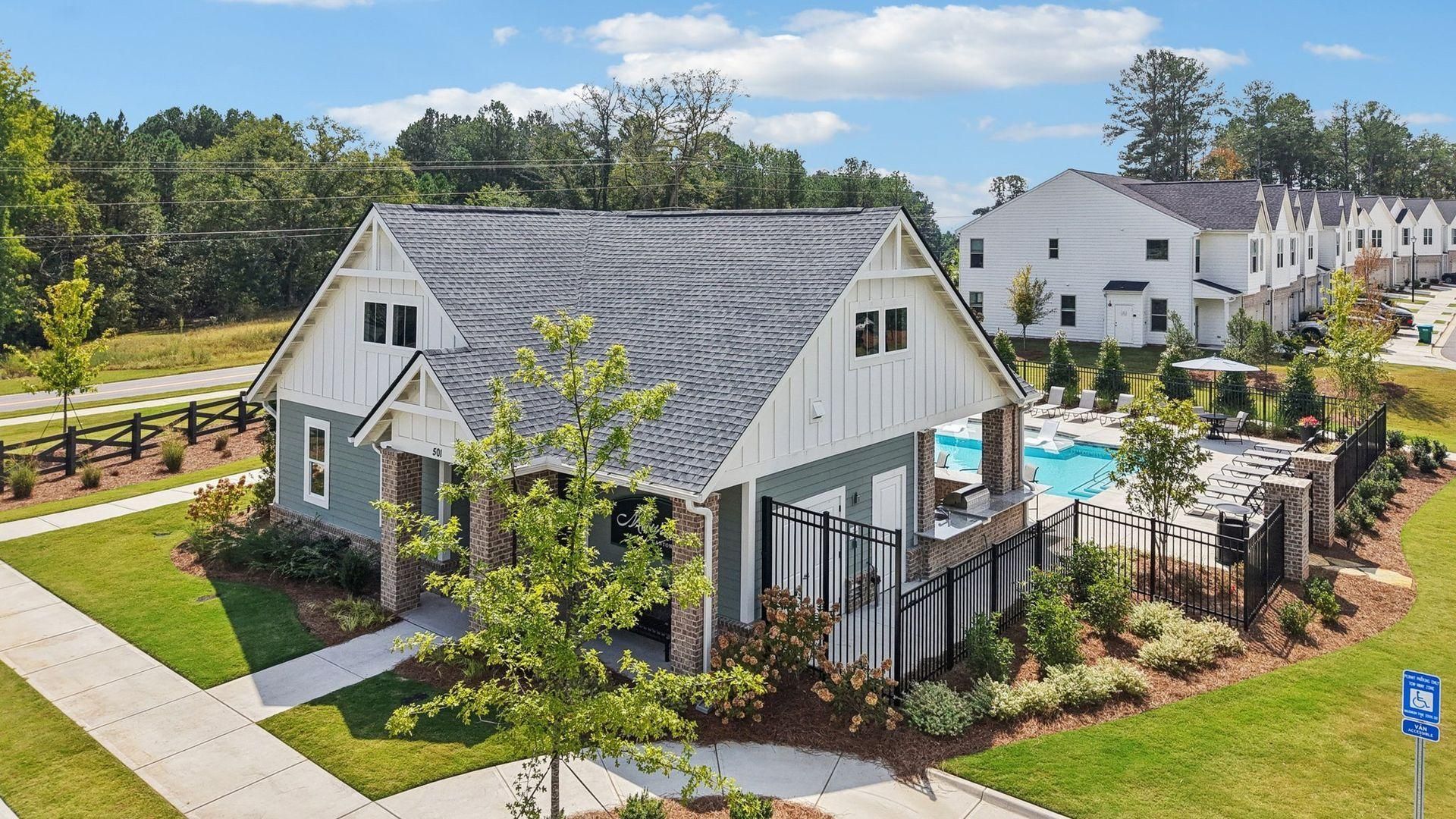 White farmhouse-style building with gray roof and patio beside a pool in a landscaped neighborhood.