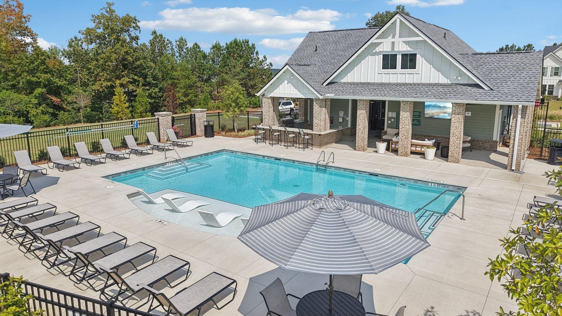 Outdoor swimming pool with lounge chairs, umbrellas, and a clubhouse under a bright blue sky