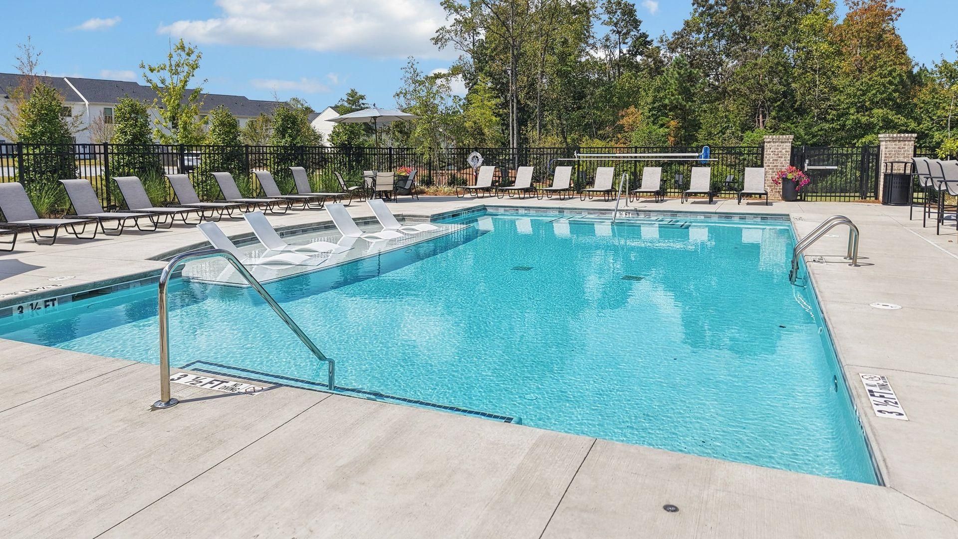 Outdoor swimming pool with clear blue water, lounge chairs, and trees in the background