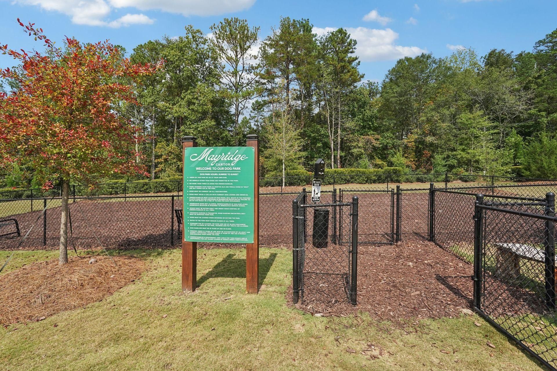 Green sign at a fenced garden plot with mulch beds and autumn trees in the background