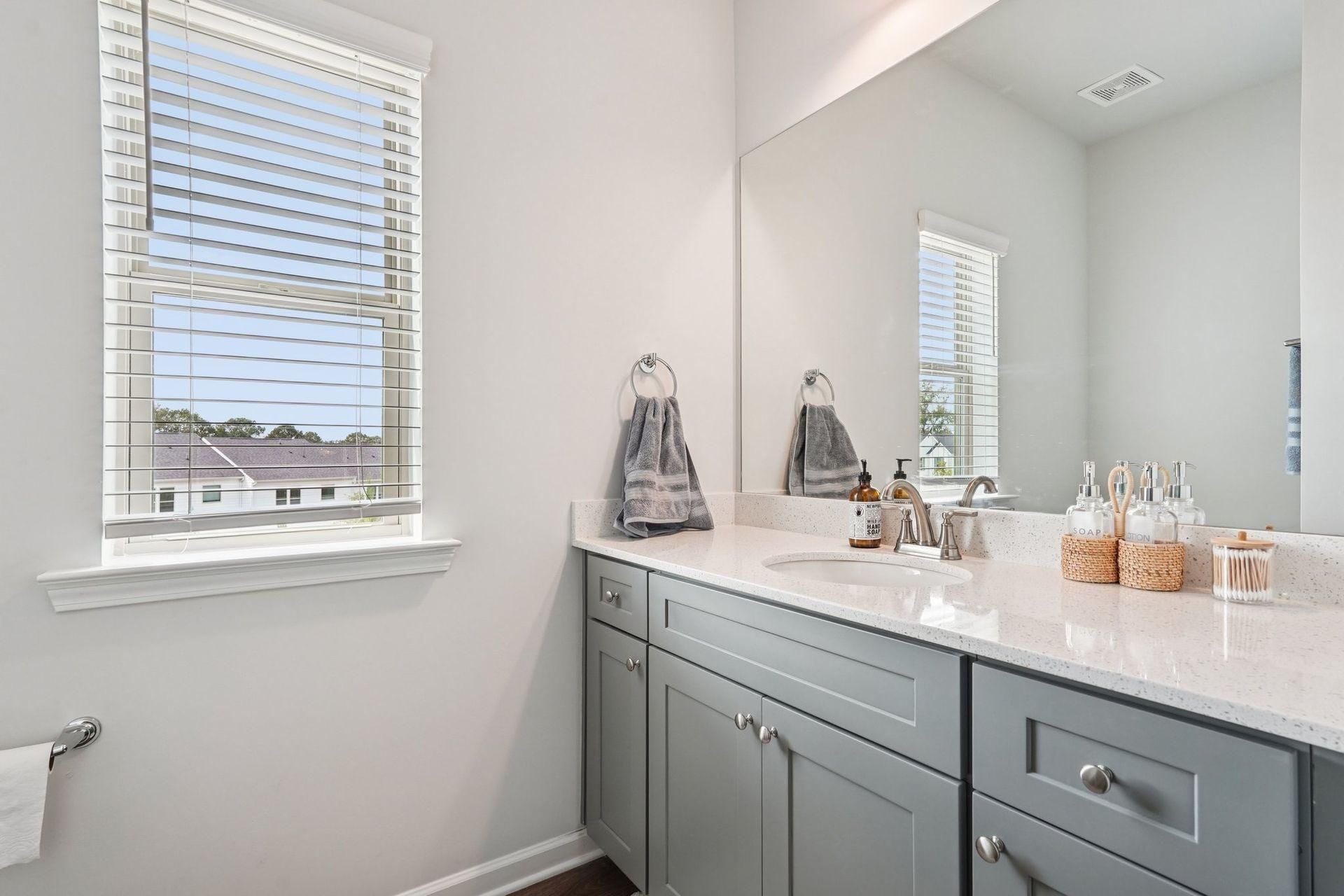 Bright bathroom vanity with gray cabinets, white countertop, and window blinds letting in daylight
