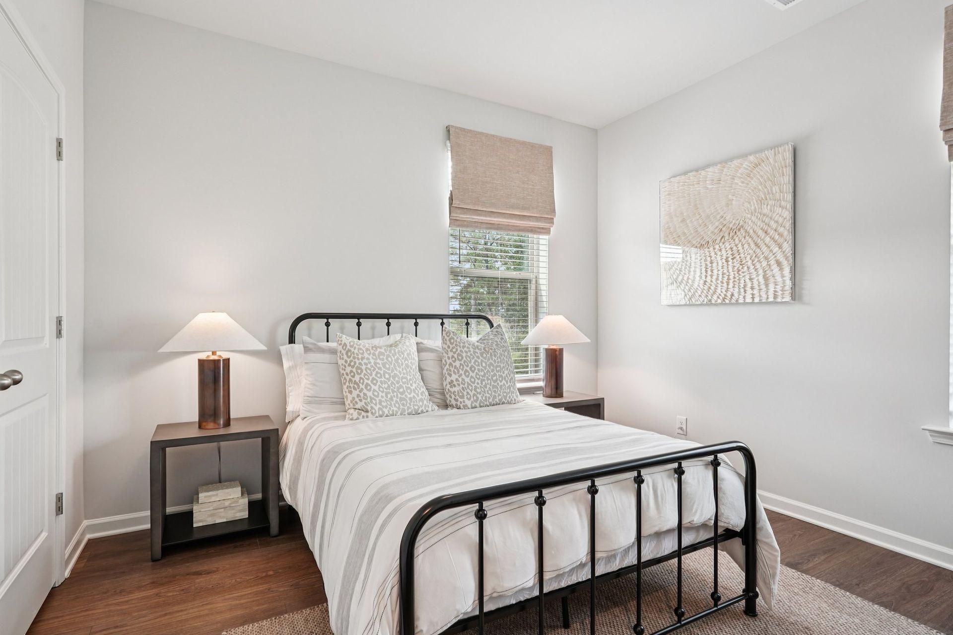 Bright bedroom with black metal bed, neutral bedding, matching lamps, and window with woven shade.
