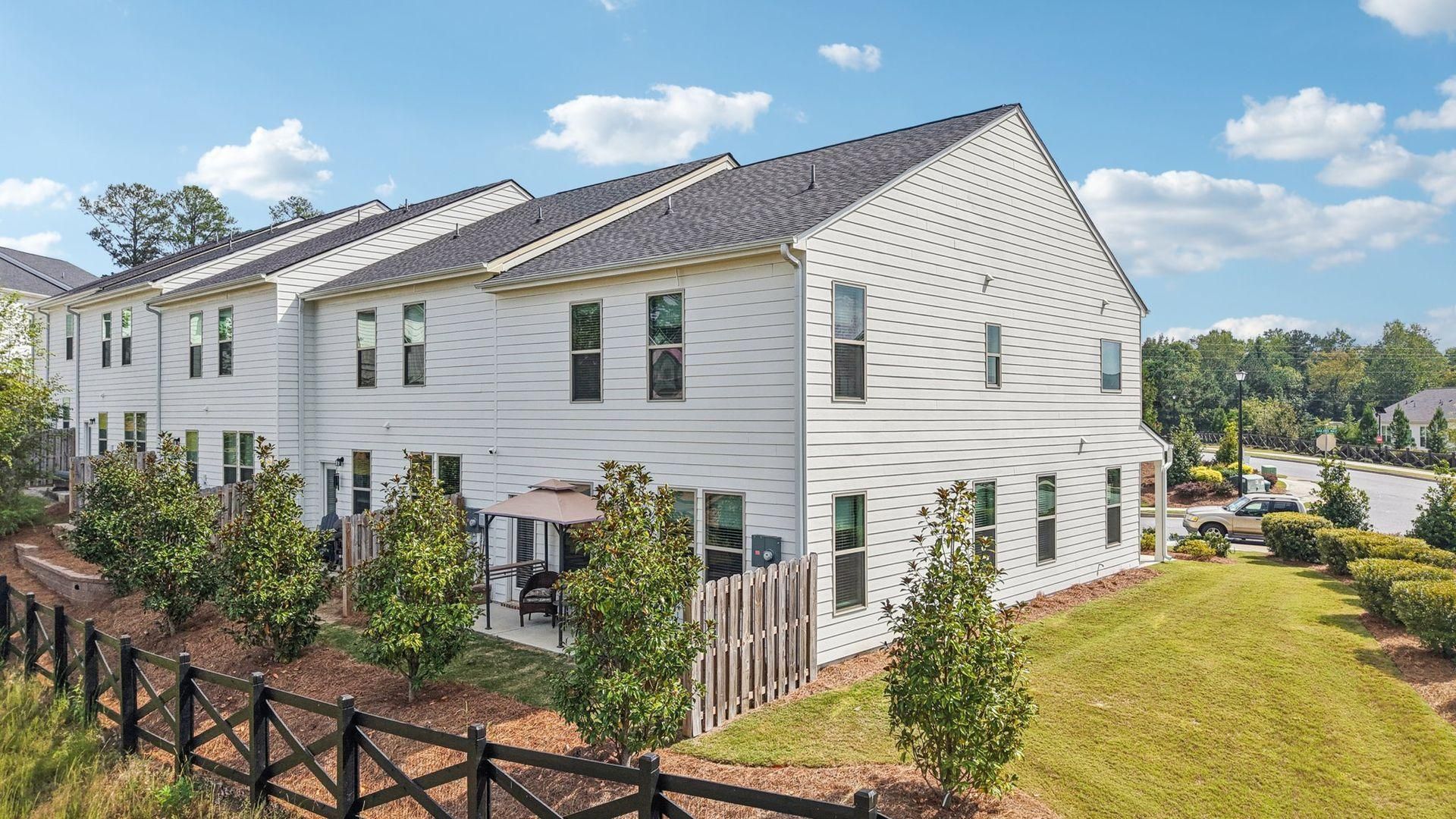 White townhouse row with black shutters, front yard landscaping, and a partly cloudy sky