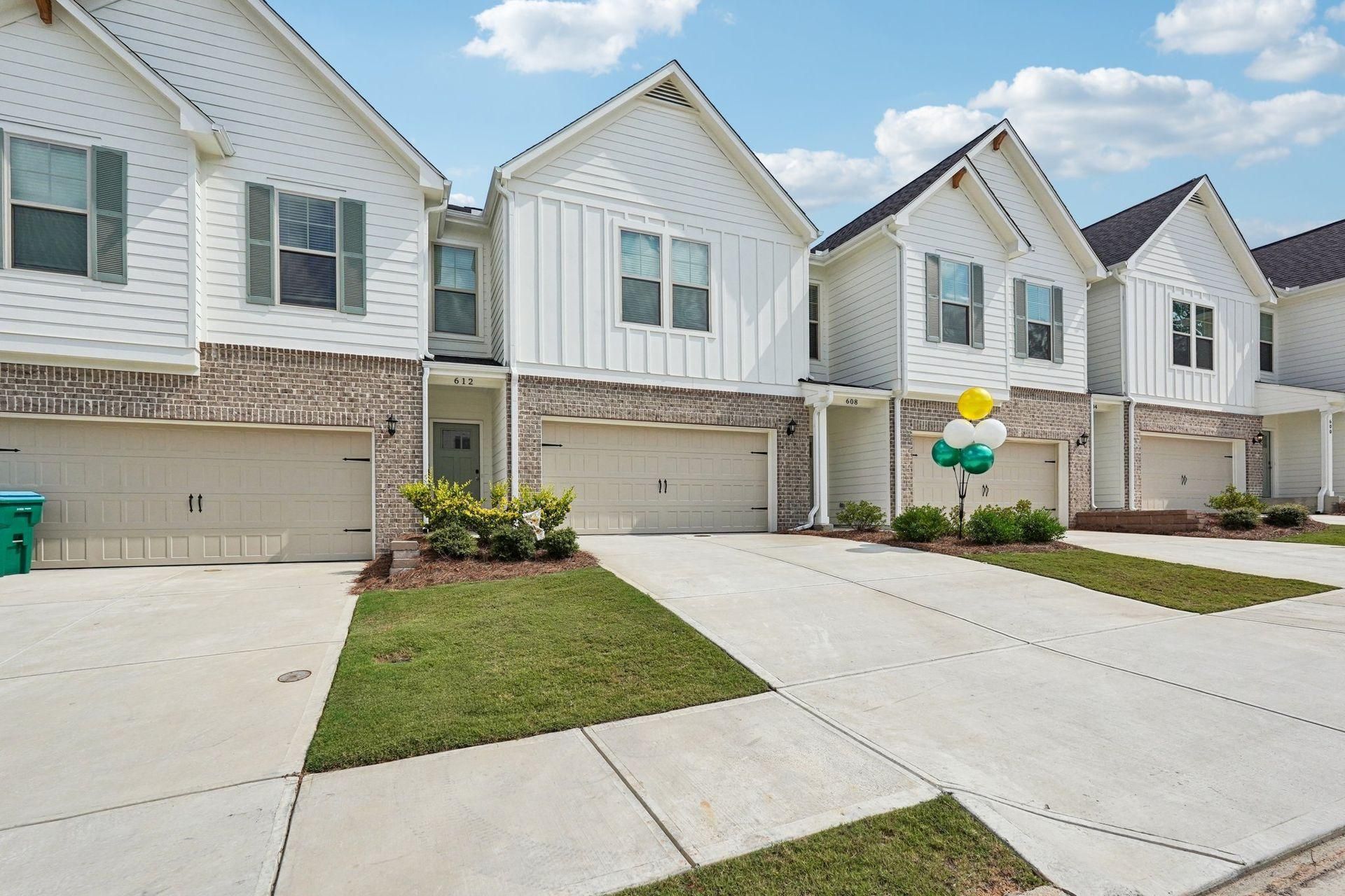 Row of modern white townhouses with attached garages and small front lawns on a sunny day