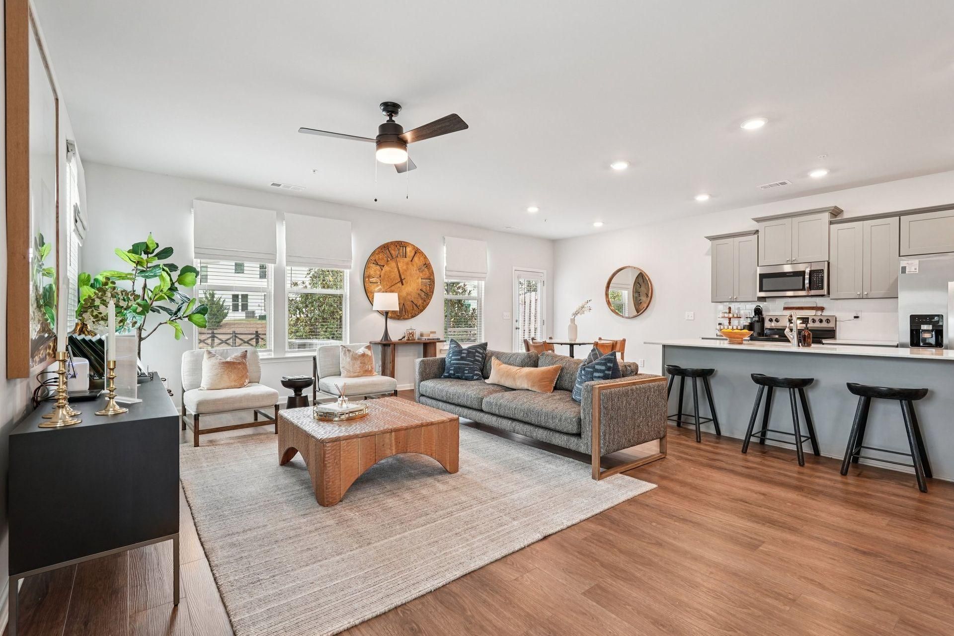 Bright open living room with gray sofas, wood floors, woven decor, and a white kitchen with bar stools