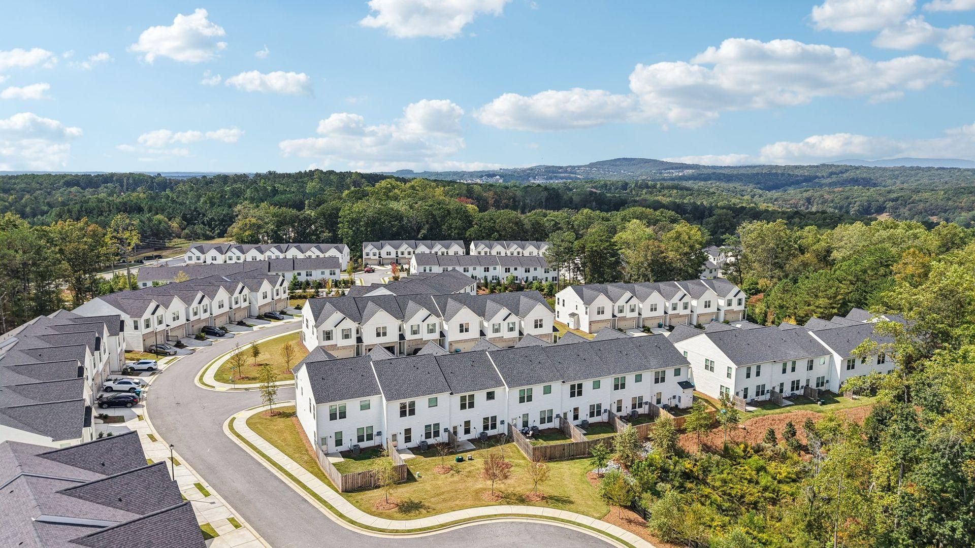 Aerial view of a large white residential apartment complex surrounded by trees under a blue sky with clouds