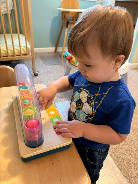 Toddler playing with a colorful wooden toy at a table in a carpeted room