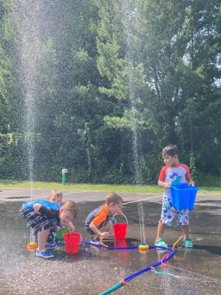 Children playing with water toys and buckets at a park fountain on a sunny day