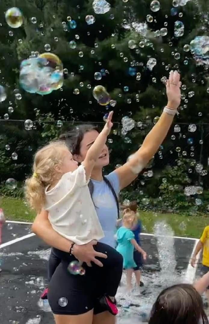 Adult and child reaching up at outdoor bubble fountain in a park