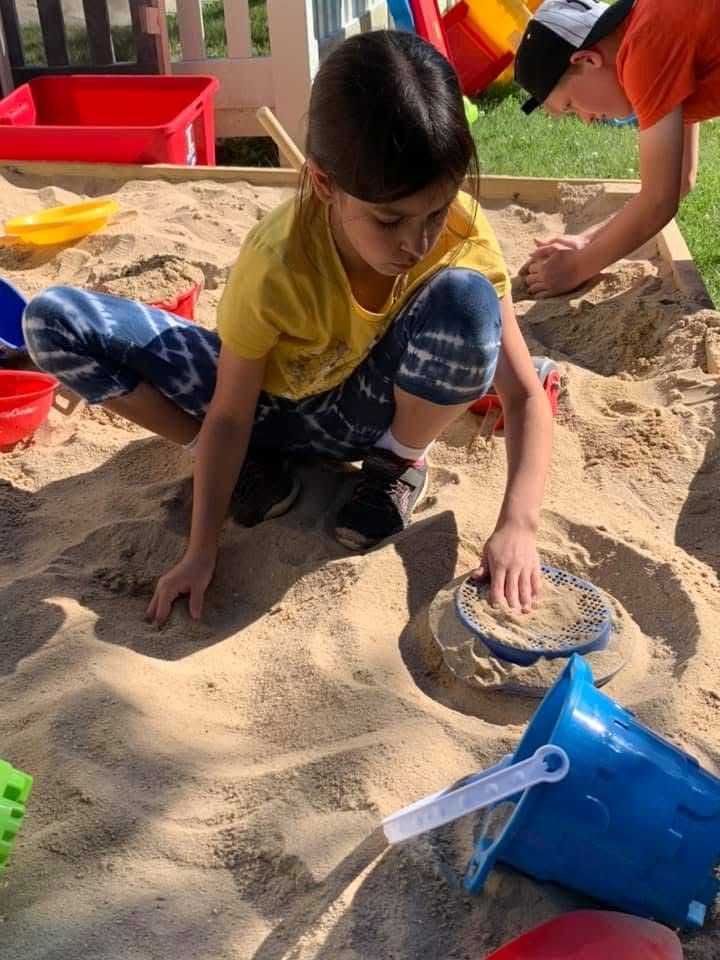Child playing in sand with colorful buckets and toys at a playground