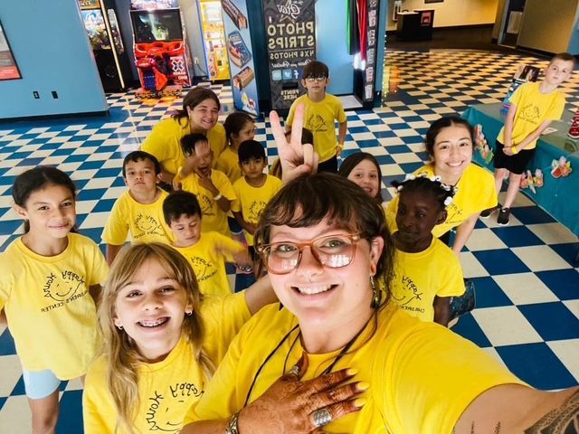 Group of children and adults in yellow shirts posing in a blue-and-white checkered indoor play area