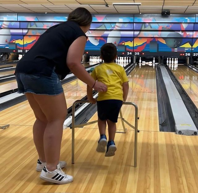 Adult guiding child with a bowling ramp at a bowling alley, aiming toward the pins.