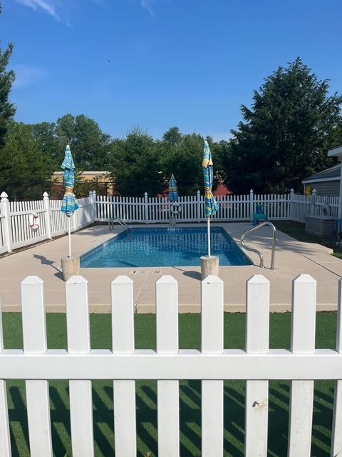Backyard pool with white fence and closed umbrella on a sunny day