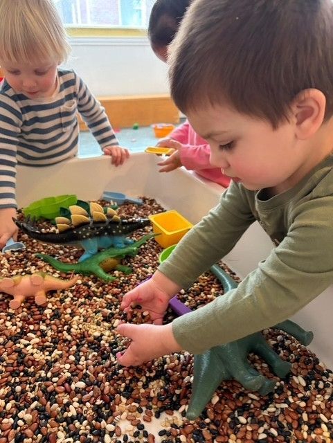 Two children play with sensory bins of beads and toy animals on a table