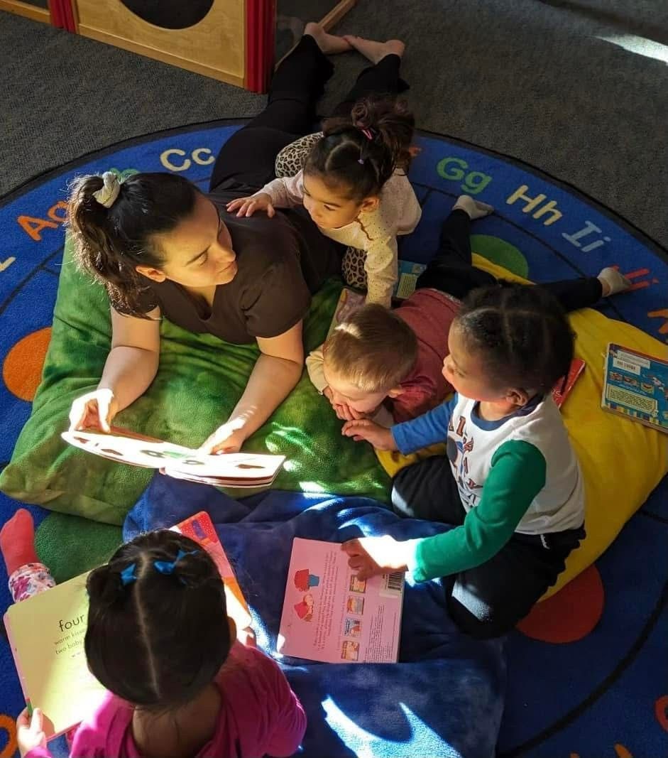 Children sitting on a colorful rug, reading a book together in a classroom.