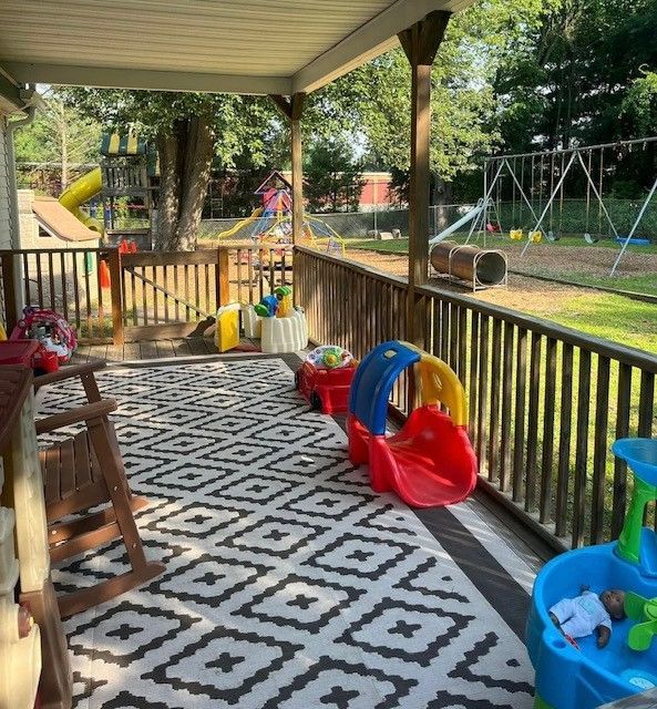 Covered porch with kids’ toys, patterned rug, and a backyard swing set beyond the railing