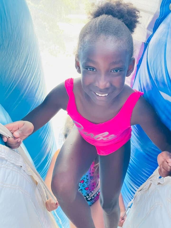 Smiling child in a bright pink swimsuit on a waterslide, holding the sides and looking up.