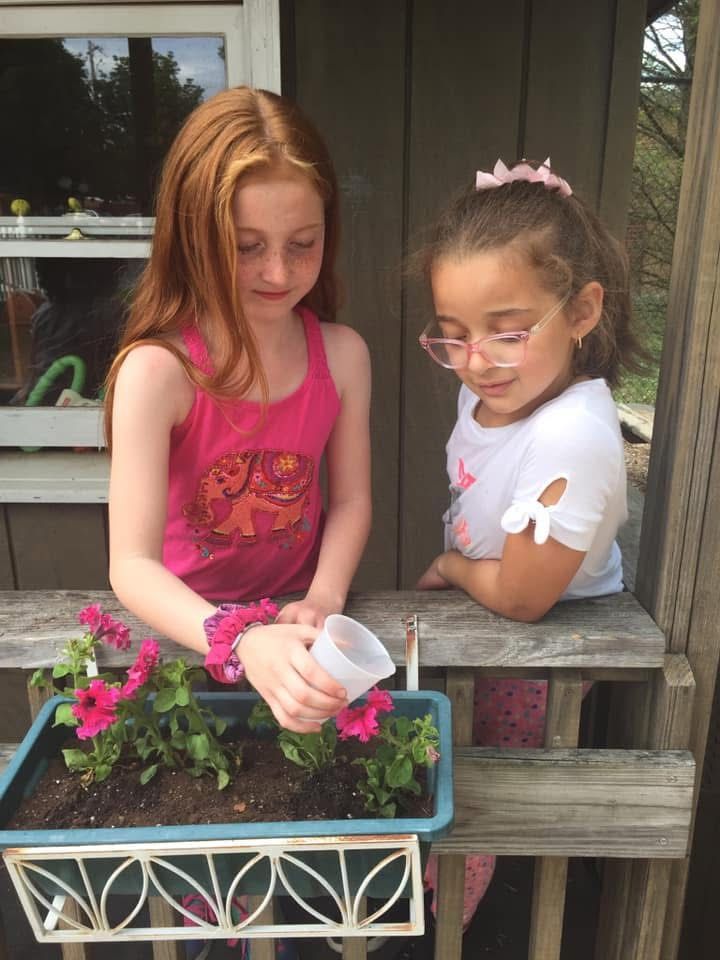 Two children watering flowers in a planter on a porch