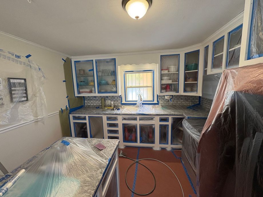 Kitchen with cabinets and appliances covered in plastic and tape, undergoing renovation.