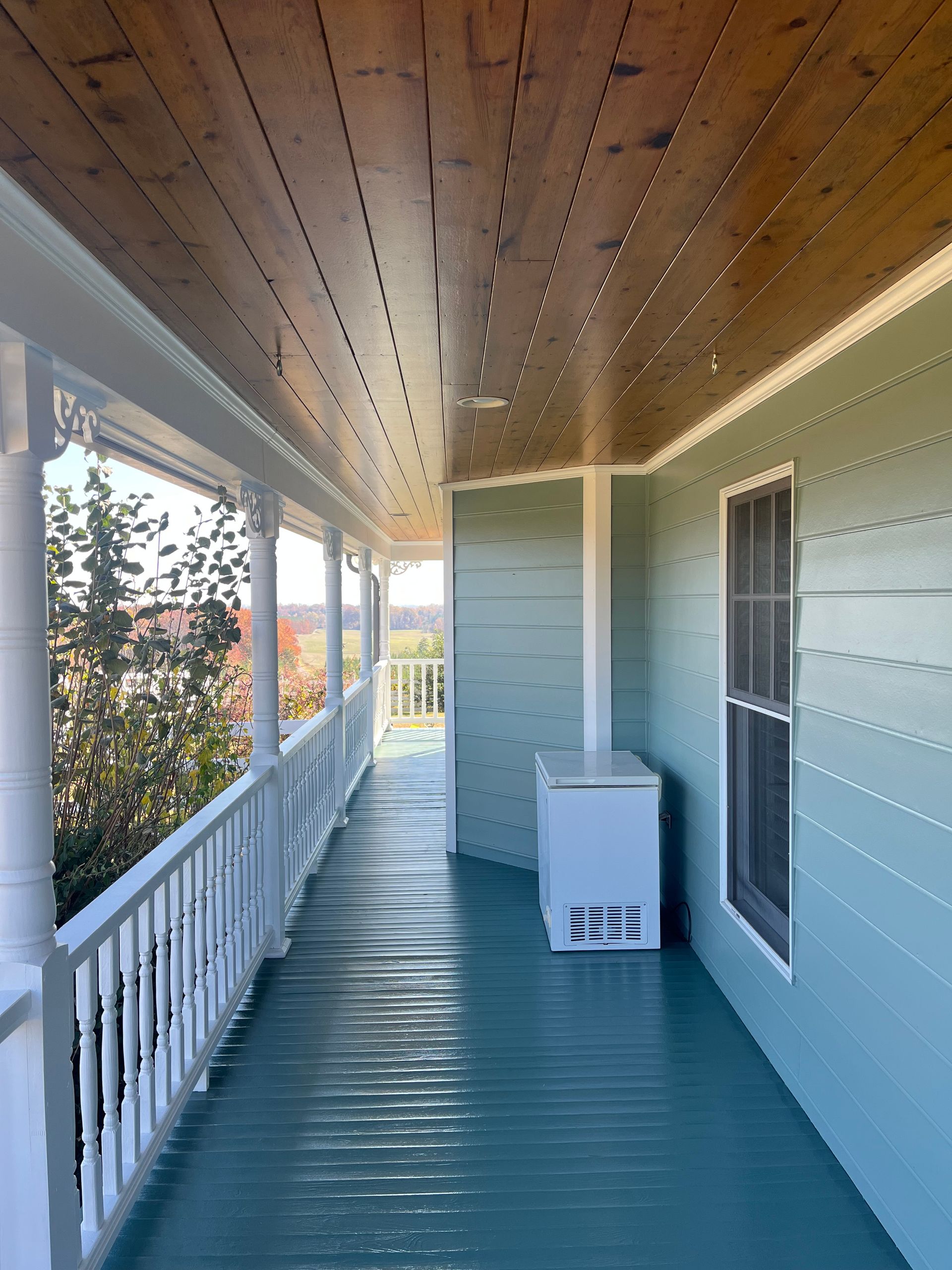 Covered porch with teal floor and light green walls, white railings, and brown wood ceiling.