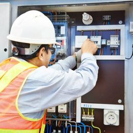 Electrician in hard hat adjusting wiring in an open electrical control panel