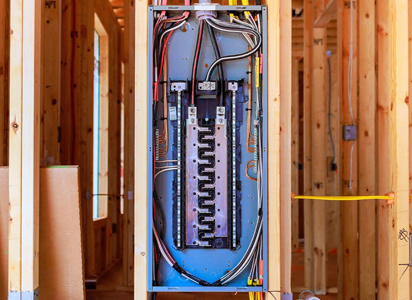 Open electrical breaker panel mounted in unfinished wood-framed wall during construction.