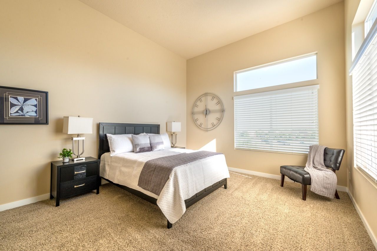Bedroom in an apartment with a bed, two nightstands, lamps, and a large window with blinds.
