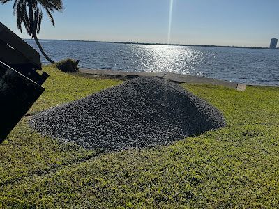 A pile of gravel is sitting on top of a lush green field next to a body of water.