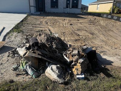 A pile of trash is sitting in the dirt in front of a house.