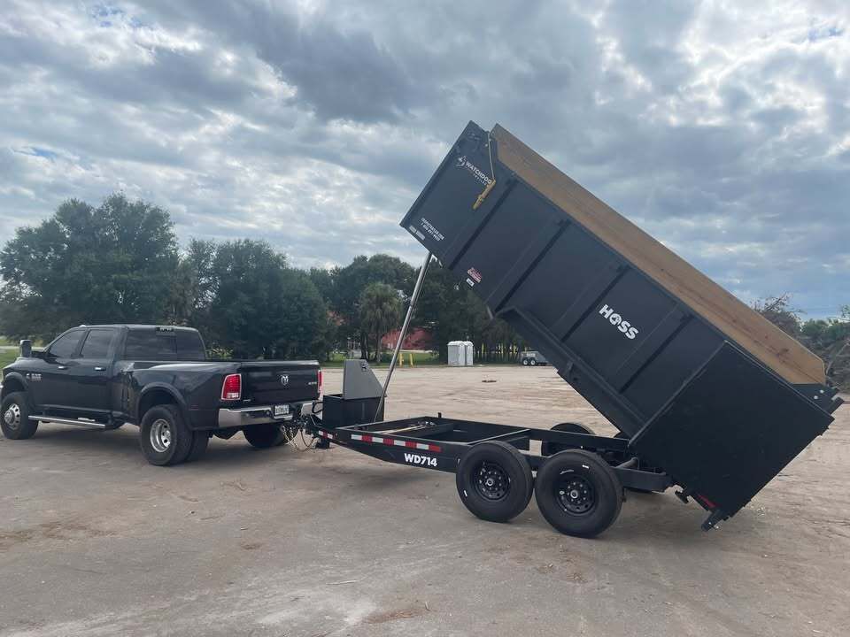 A dumpster is being towed by a truck in a parking lot