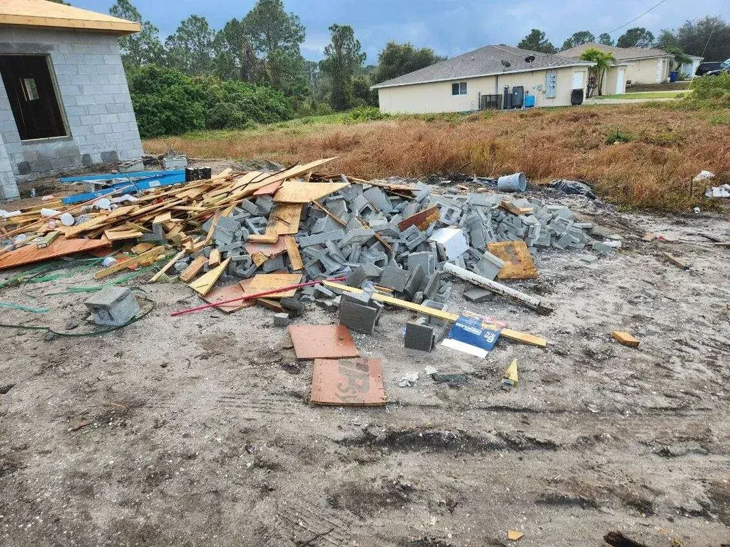 A pile of rubble is sitting in the dirt in front of a house under construction.