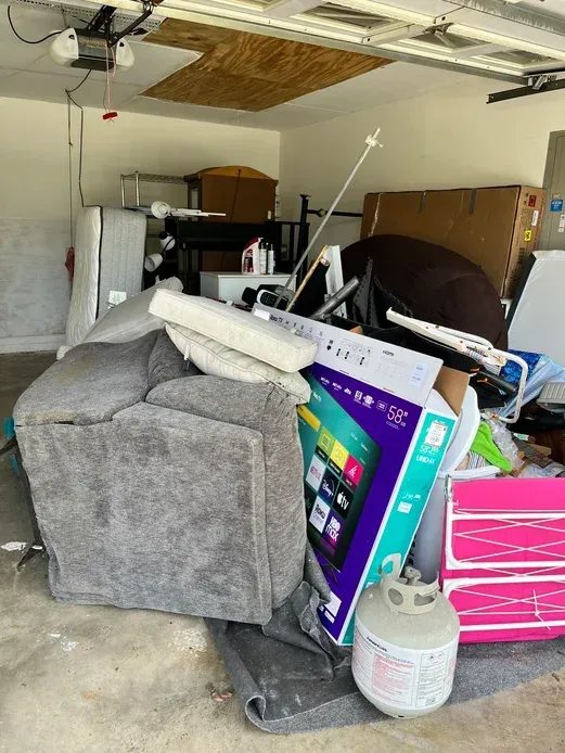 A garage filled with a lot of junk , including a couch and a television.