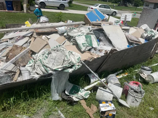 A pile of trash is sitting in the grass in front of a house.