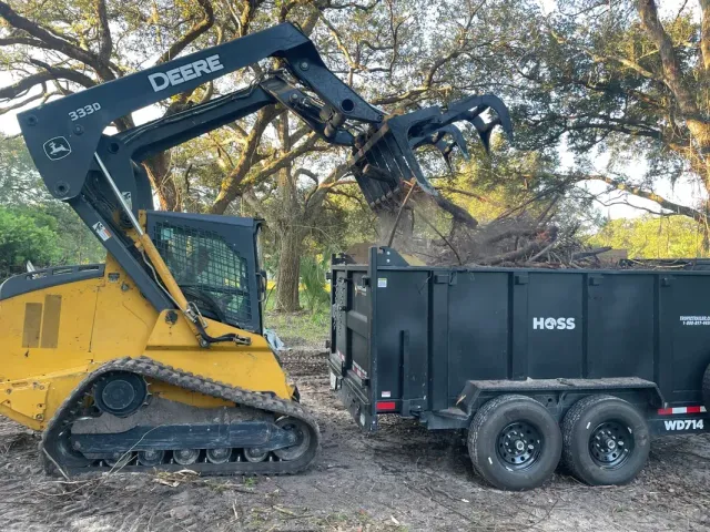 A bulldozer is loading a dumpster into a trailer.