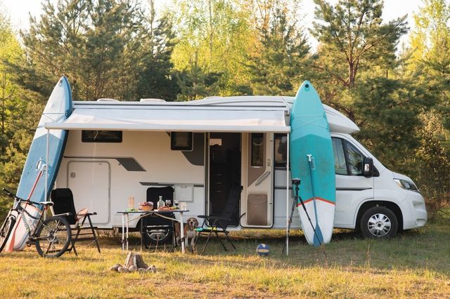 A rv with surfboards attached to the side is parked in a field.