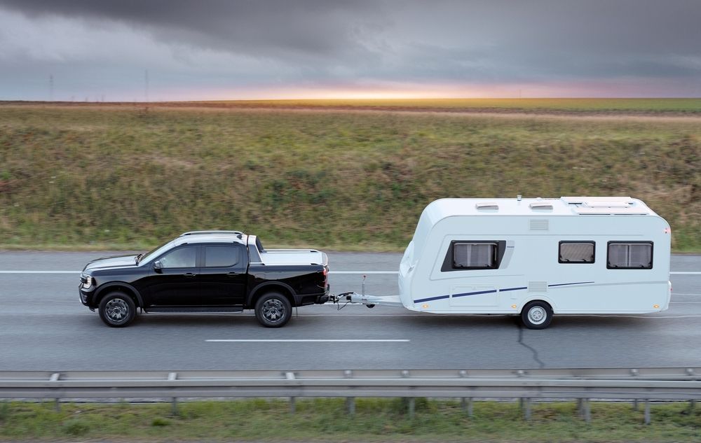 A black truck is towing a white trailer on a highway.