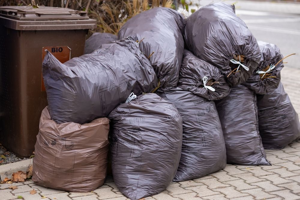 A pile of garbage bags sitting on the sidewalk next to a trash can.