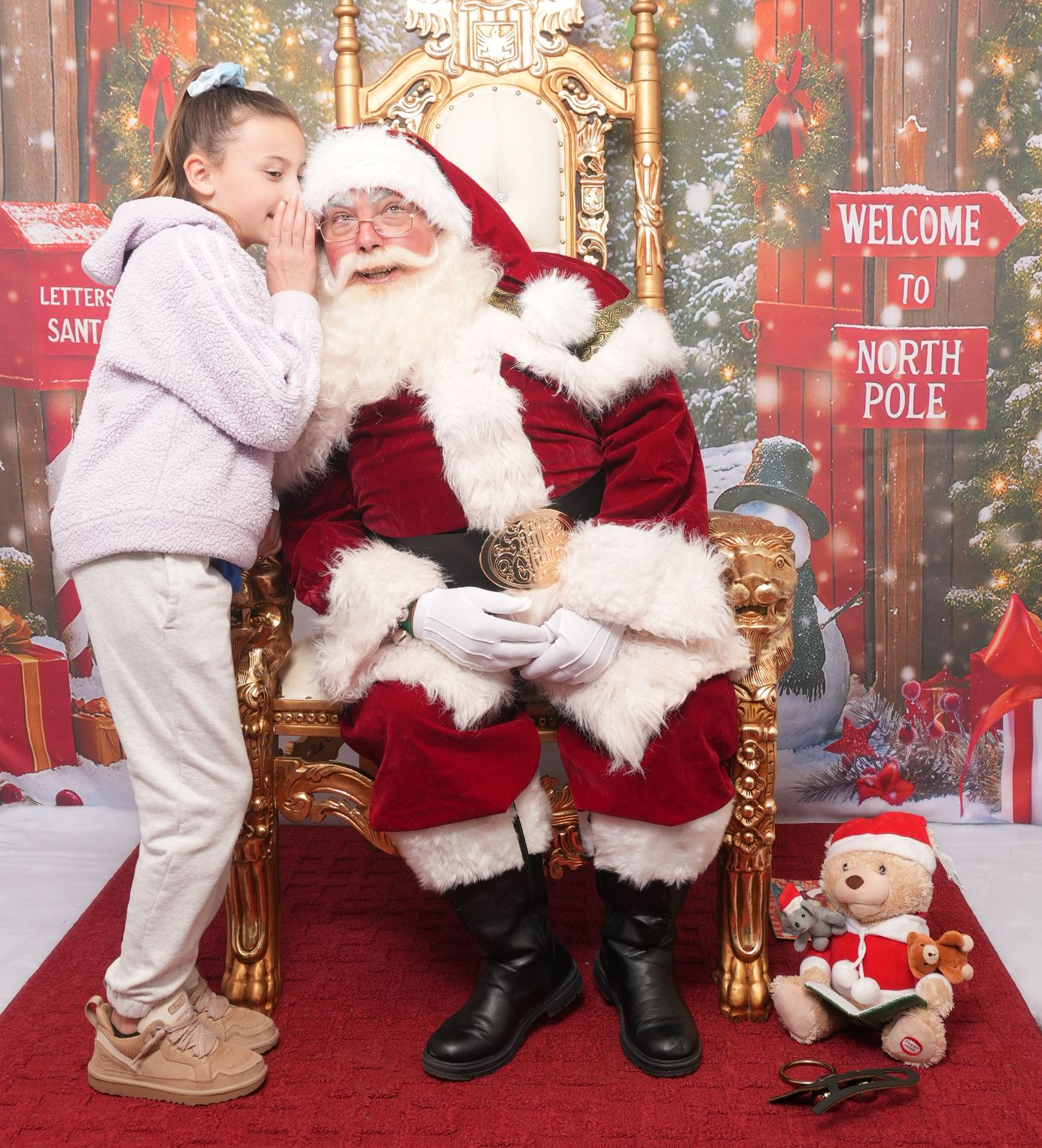 Girl whispering into Santa's ear while he sits on a throne. Christmas scene, red and white.