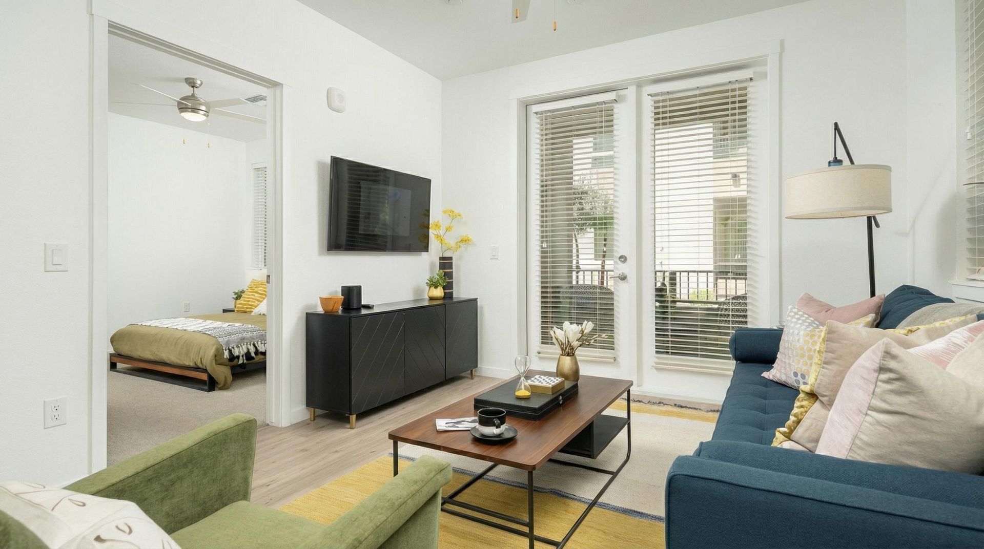 Bright living room in an apartment with blue sofa, green chair, coffee table, and balcony doors.