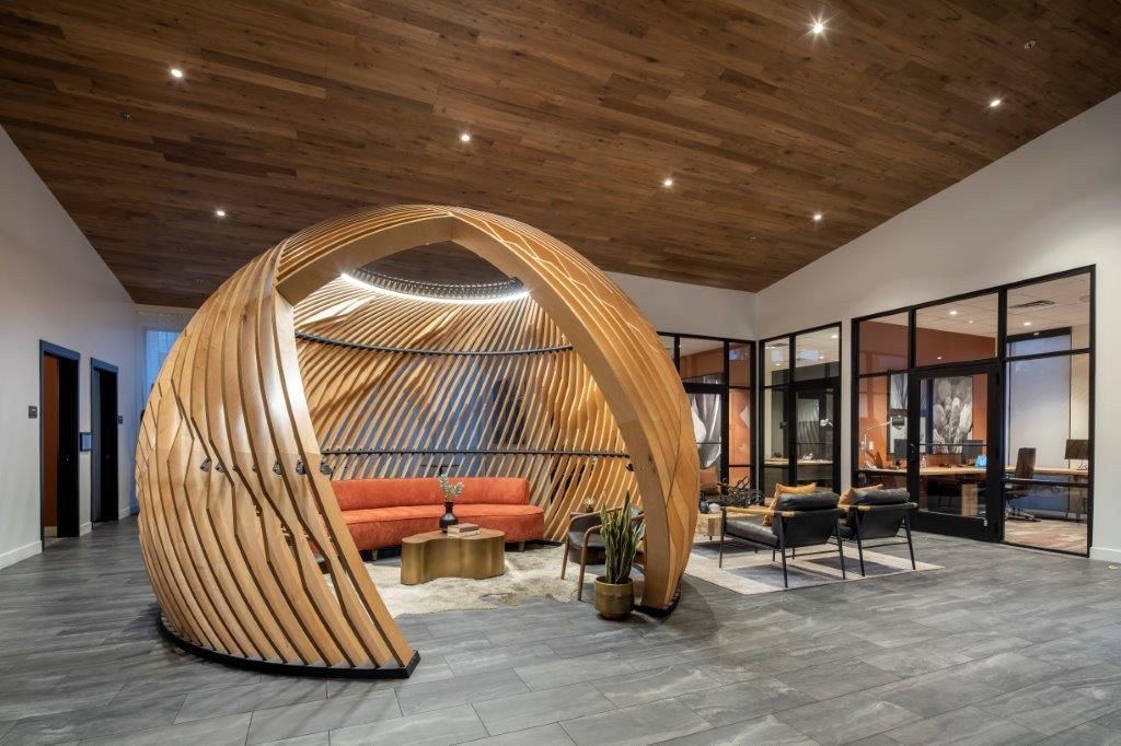 Modern lobby area featuring a large curved wooden seating pod and glass-walled meeting rooms at Aiya, offering luxury apartments in Gilbert, AZ.